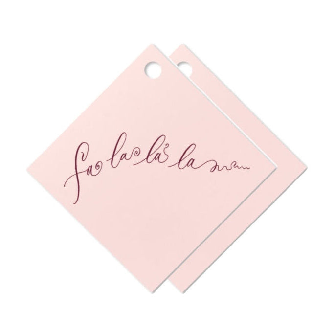 Two square light pink cards with hanging holes, overlapping on a white background. The front card features the phrase 'fa la la la mmm' printed in a dark burgundy cursive script.